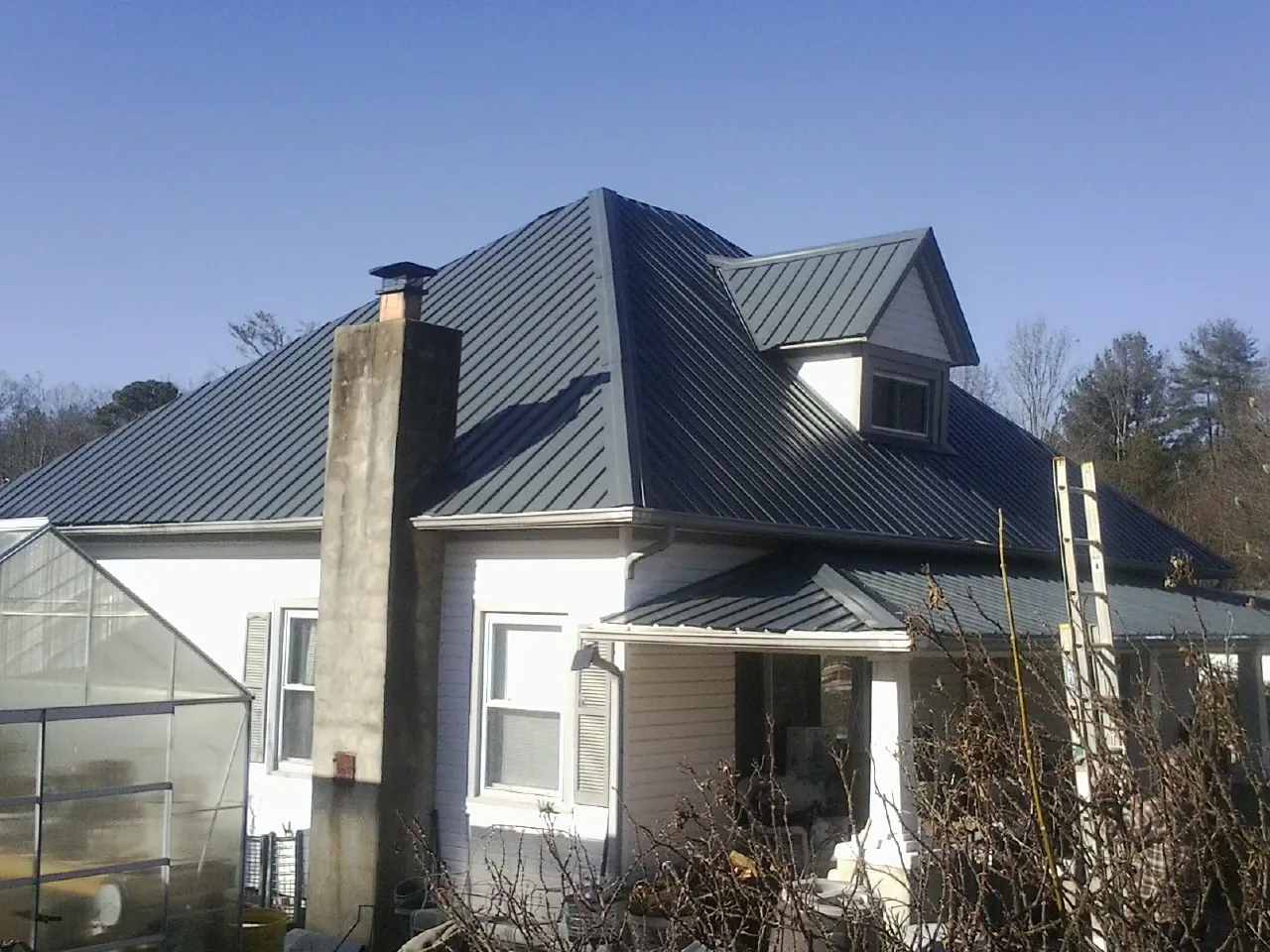 Dark blue standing seam metal roof on a white farmhouse with dormer — Slate & Tile Roof Repair by Roofing Brothers in Belding