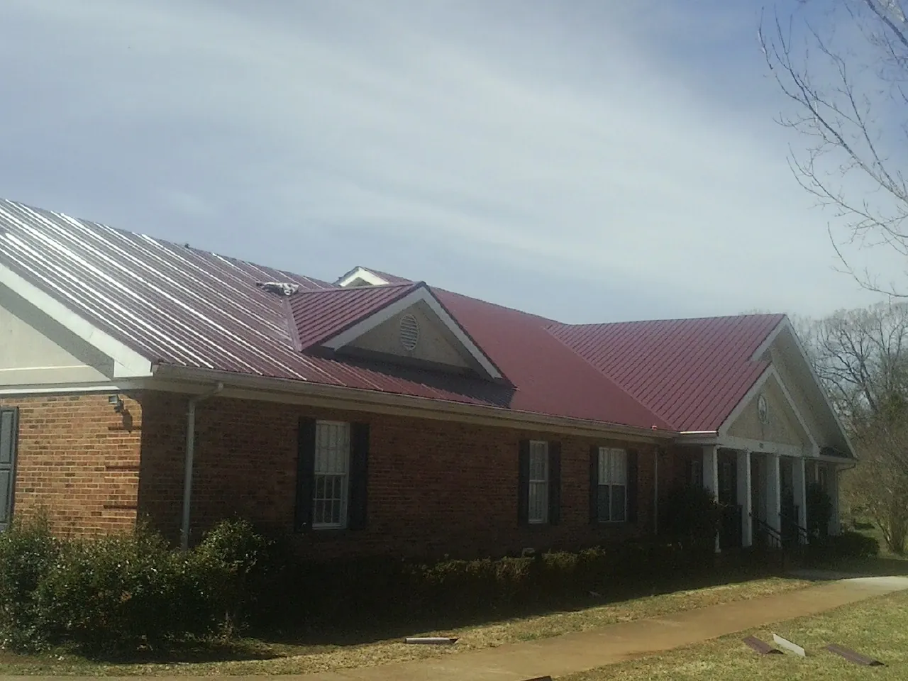 Red metal roof with gabled entries on a long brick building, from a Hail Damage Roof Repair job in Belding