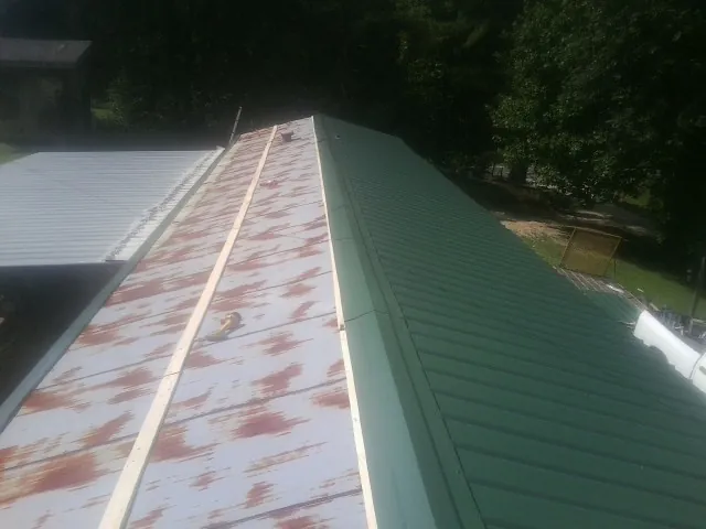 Old rusted panels beside newly installed green metal roofing — Wind Damage Roof Repair by Roofing Brothers in Belding