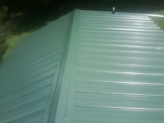 New green metal panels meeting at the ridge of a roof — Flat Roof Repair work by our crew in Belding