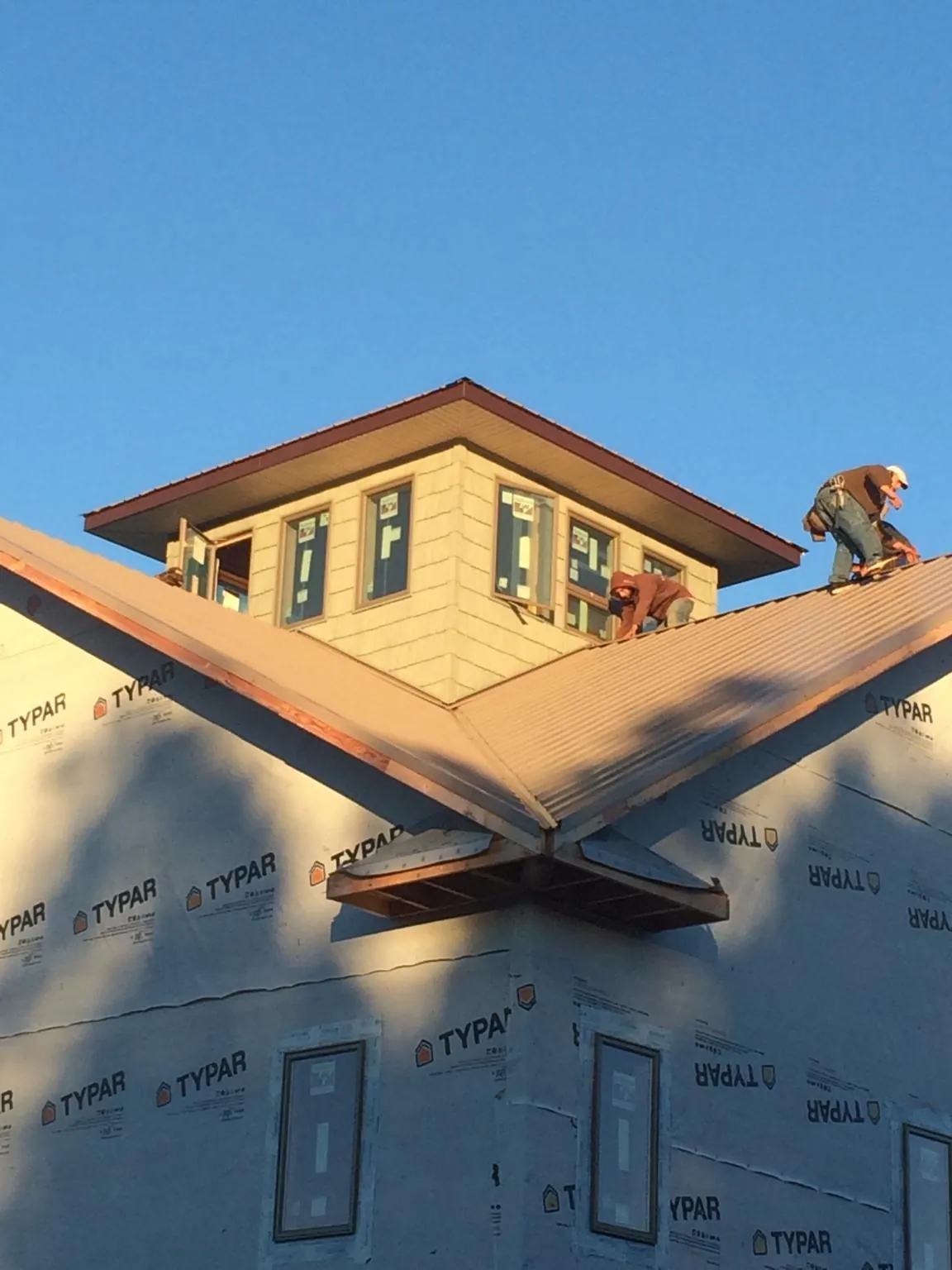 Roofers working around a rooftop cupola on a new metal roof at sunset — Roof Waterproofing in Belding by Roofing Brothers